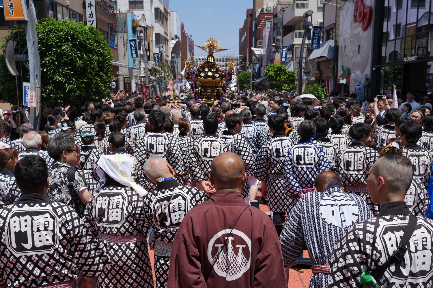 Crowded street festival with participants wearing matching black and white checkered happi coats and portable shrine