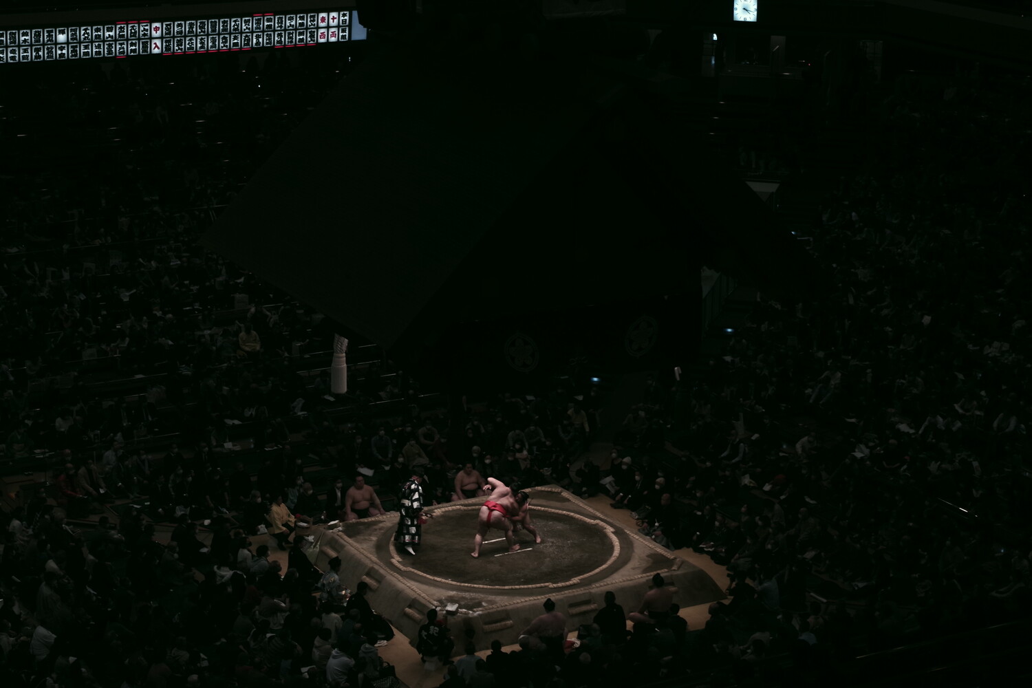 Sumo wrestlers competing in an elevated ring surrounded by spectators in a darkened arena