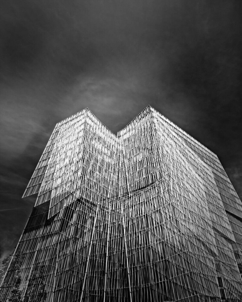 Modern high-rise building photographed from below against dramatic dark sky in black and white