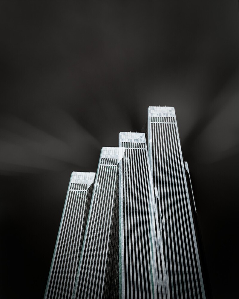 Tall vertical buildings with ribbed facades converge toward sky in dramatic black and white architectural composition