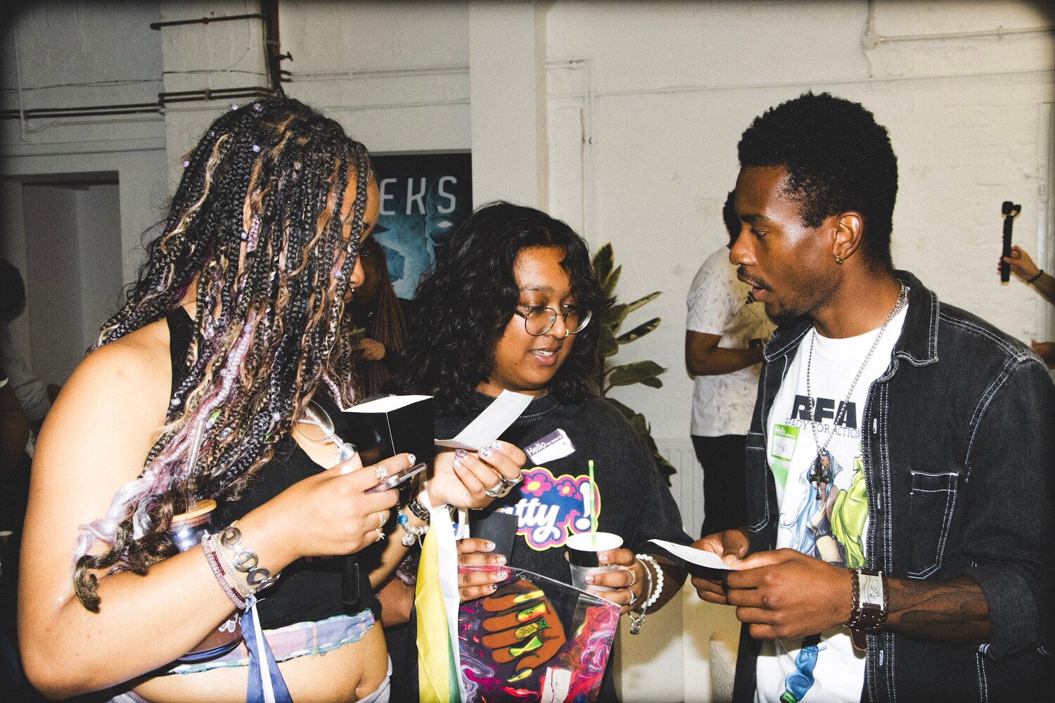 Four people at an indoor event, one signing autographs while others observe and hold merchandise