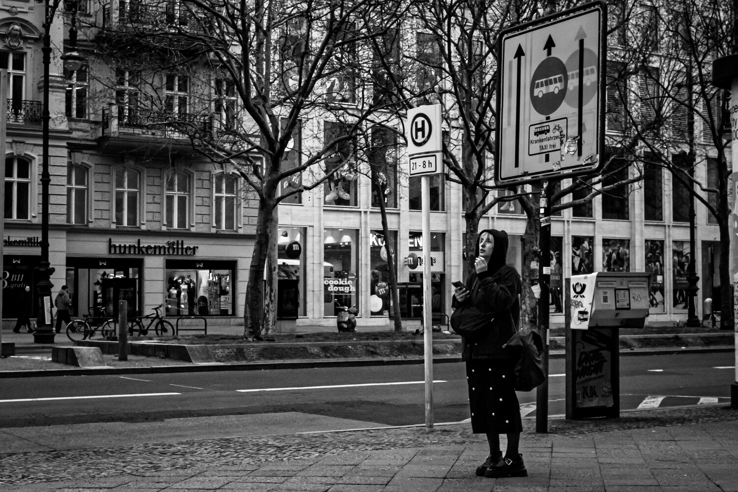 Person in dark coat standing on urban street corner beside traffic sign pole