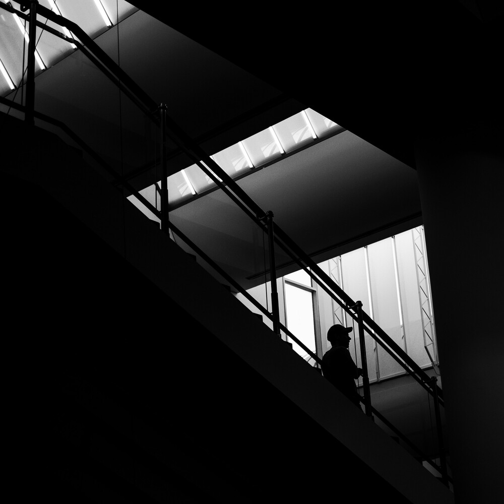 Silhouetted figure standing on industrial metal staircase with geometric shadow patterns