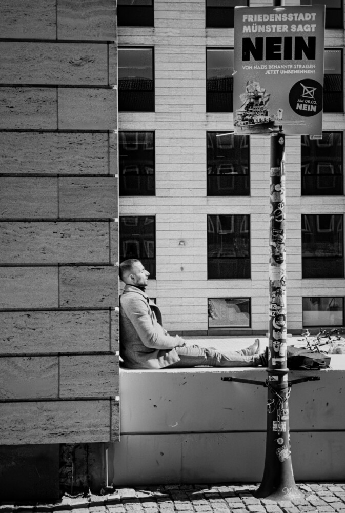 Person sitting against concrete building wall in black and white street photography