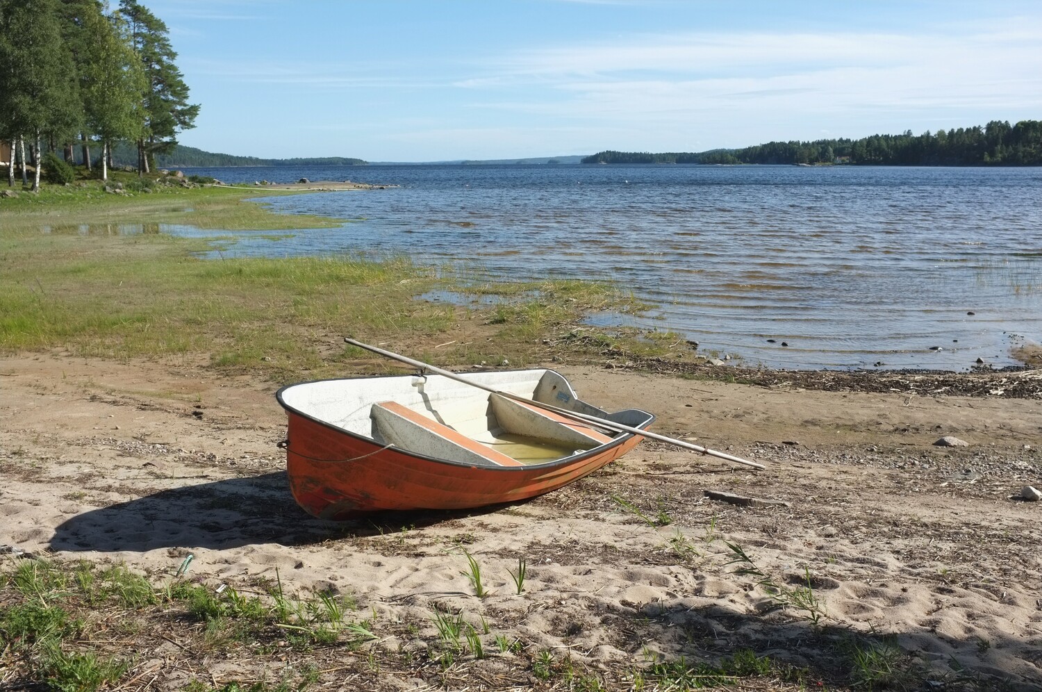 Red rowboat with oars beached on sandy shore beside calm lake
