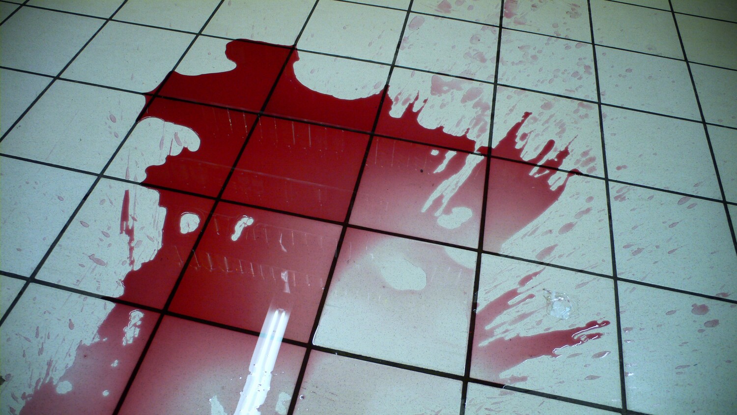 Red liquid splattered across white tile floor with grid pattern