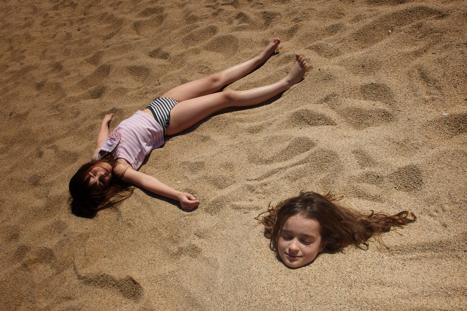 Two children lying on sand in relaxed poses during daytime