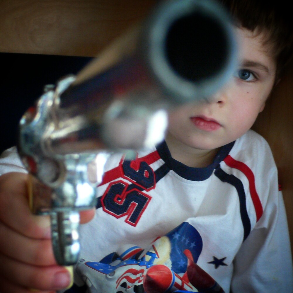 Young child holding a toy gun up to his eye, looking through the barrel
