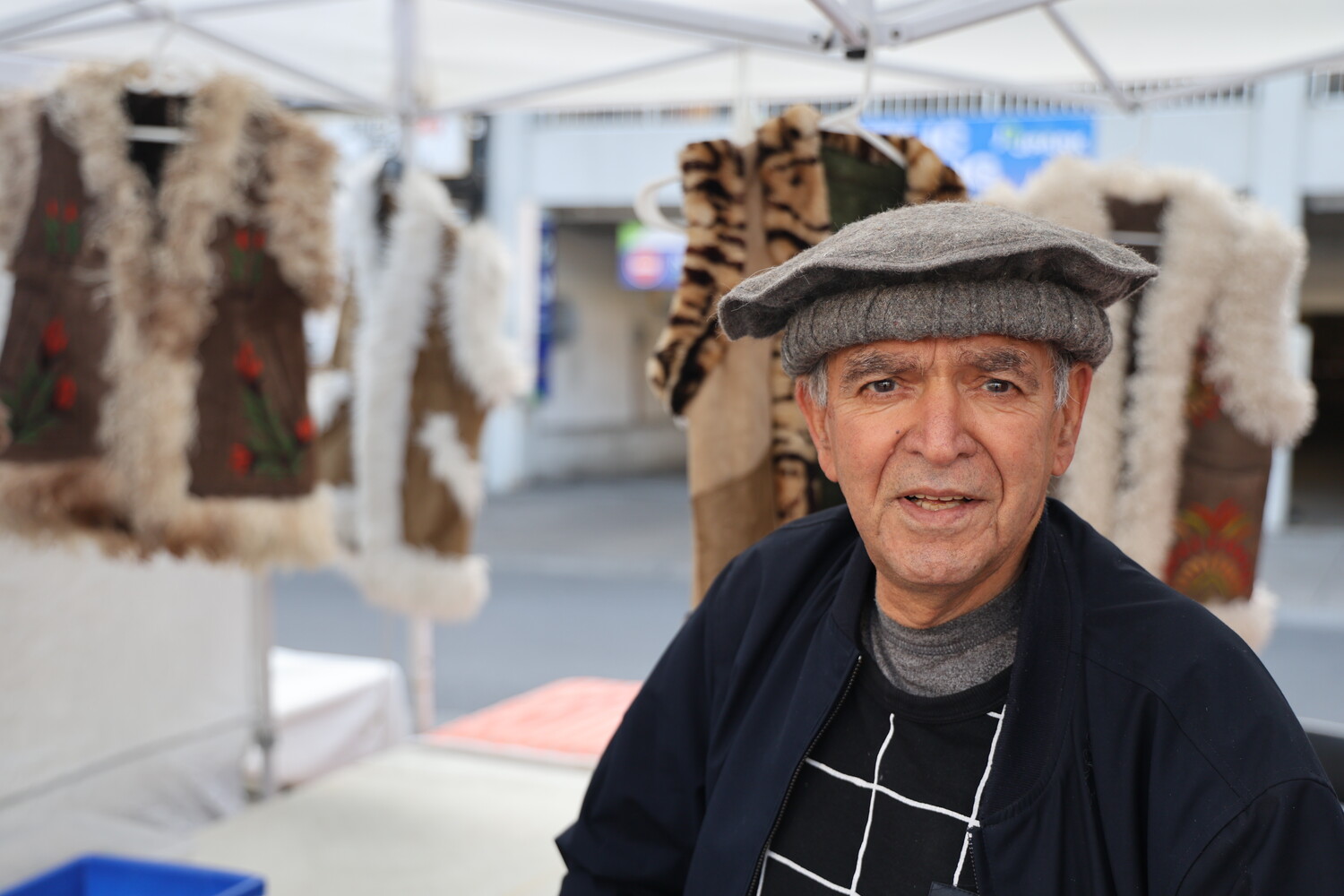 Man wearing gray flat cap and dark jacket stands in front of hanging textile artworks in gallery space
