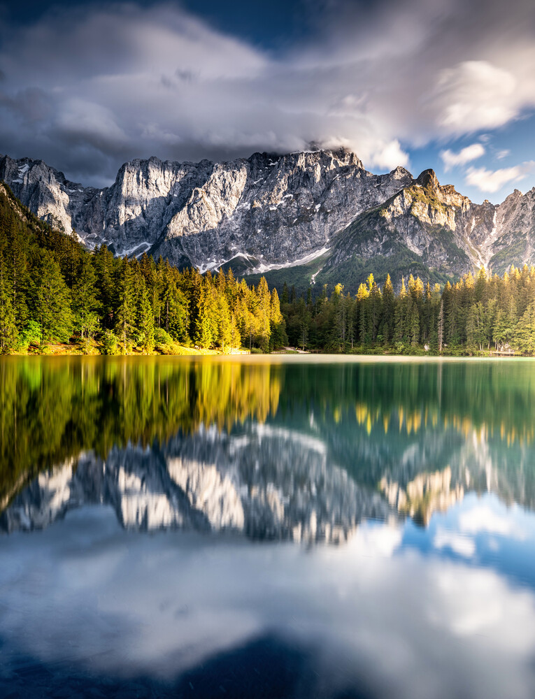 Alpine lake with mirror-like reflections of snow-capped mountains and evergreen forest