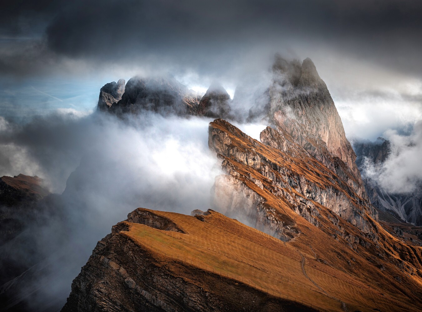 Dramatic alpine peak shrouded in swirling clouds and mist with warm golden-brown rock face in foreground