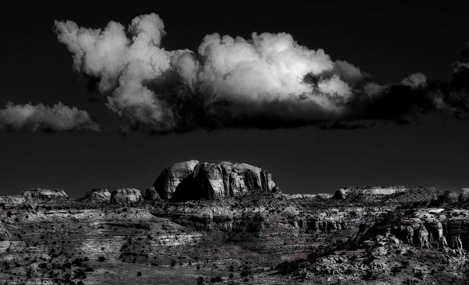 Dramatic black and white desert landscape with towering rock formation under stormy clouds