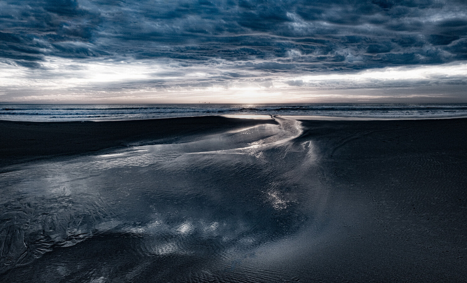 Dramatic coastal landscape with dark sand, winding water channel, and stormy sky