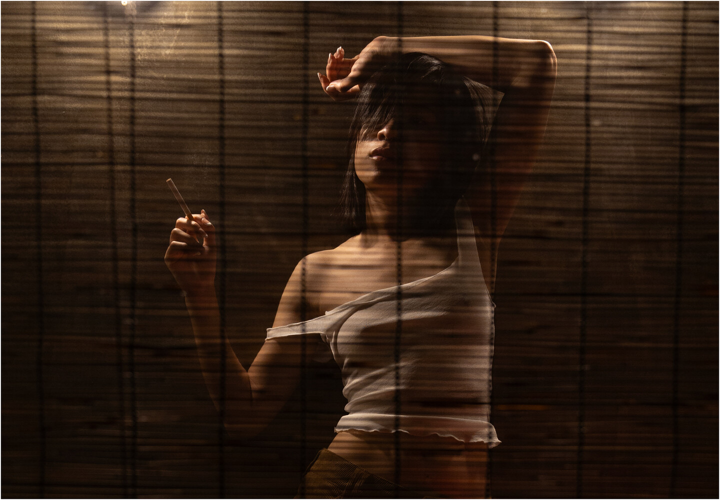 Woman in white off-shoulder top poses behind venetian blinds with dramatic side lighting