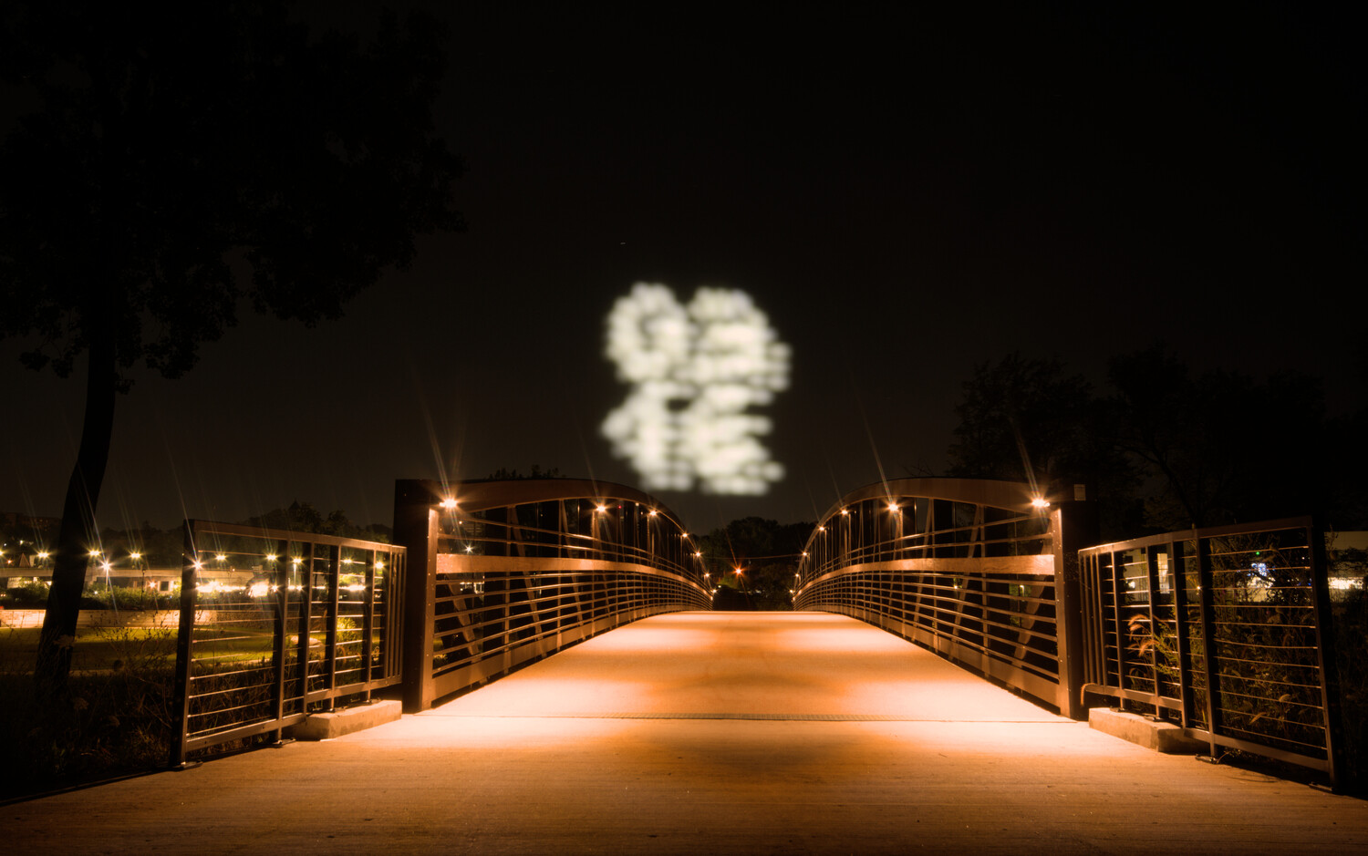 Illuminated pedestrian bridge at night with fireworks exploding in the sky above
