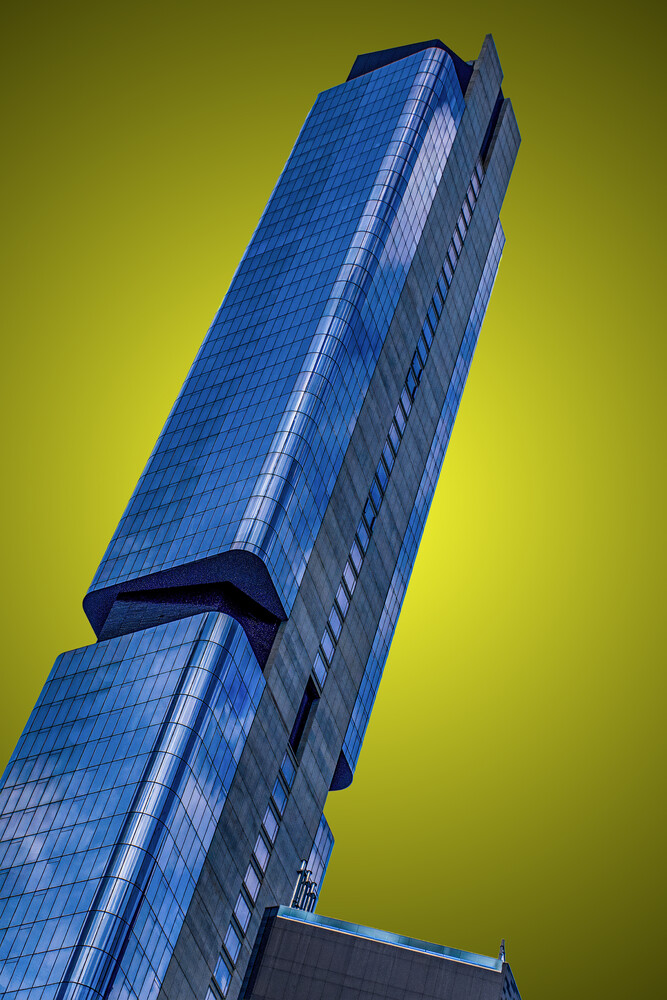 Modern blue glass skyscraper photographed from below against a yellow-green sky
