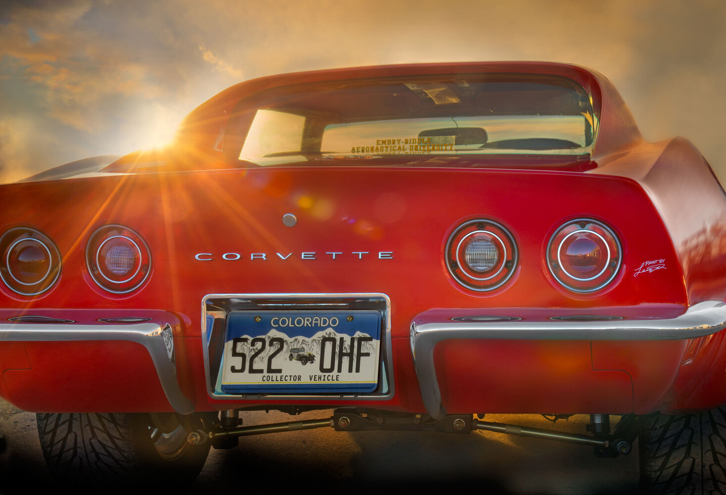 Rear view of a red classic Corvette at sunset, with sunlight flaring through the rear window and a Colorado collector plate.