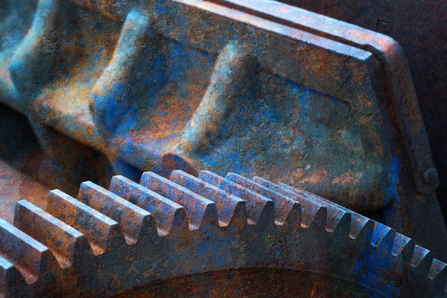 Close-up of rusted metal gear teeth with blue and orange patina on a weathered industrial housing