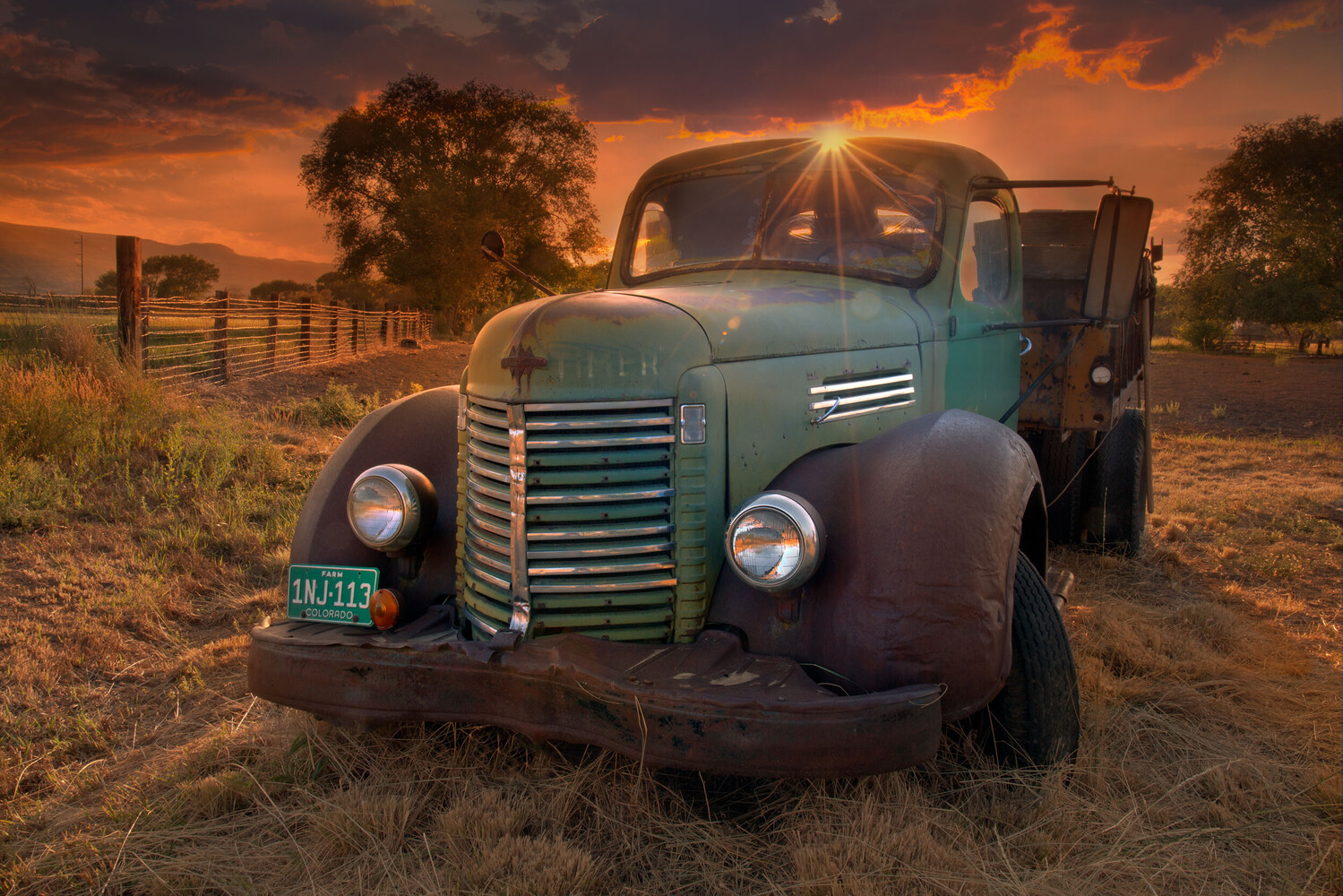 Rusted vintage green truck parked in dry grass, with the sun flaring through the windshield at sunset.