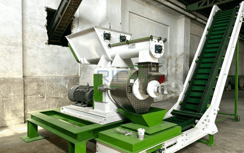 Industrial pellet mill with green frame and white components mounted on concrete floor