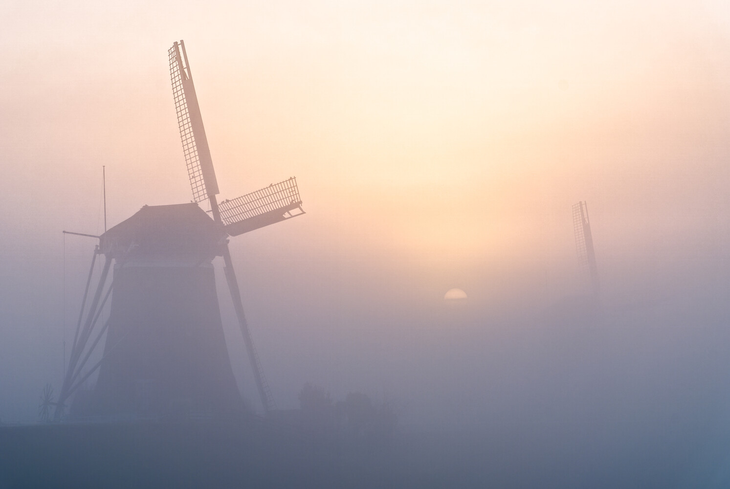 Traditional Dutch windmill silhouetted against a misty sunrise