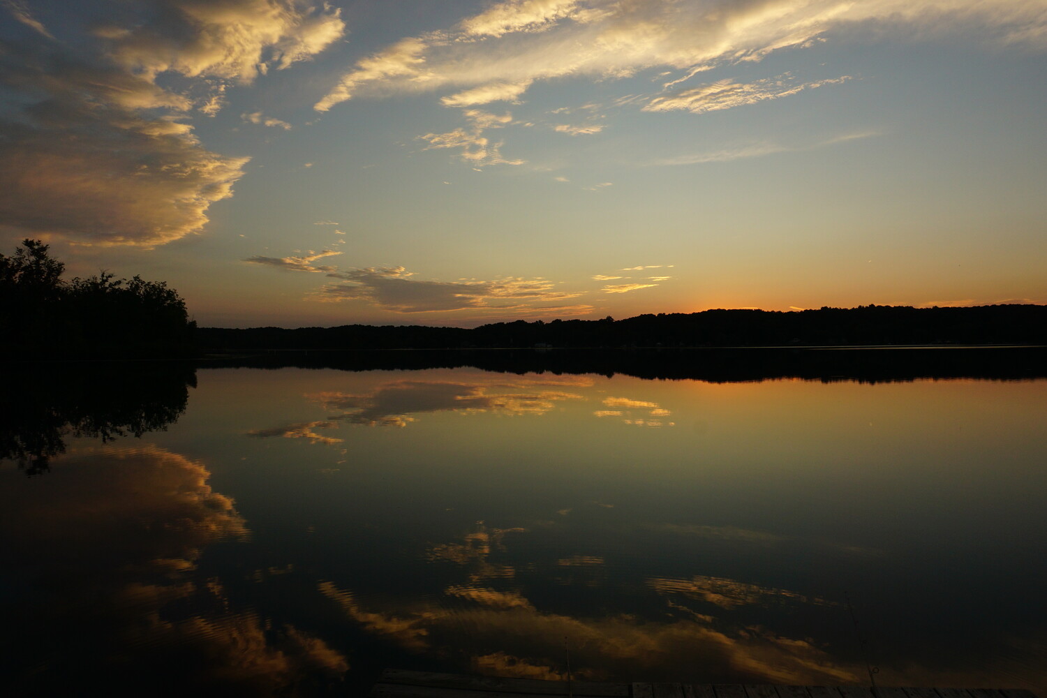 Calm lake at sunset with golden clouds reflecting on still water and forested shoreline in silhouette