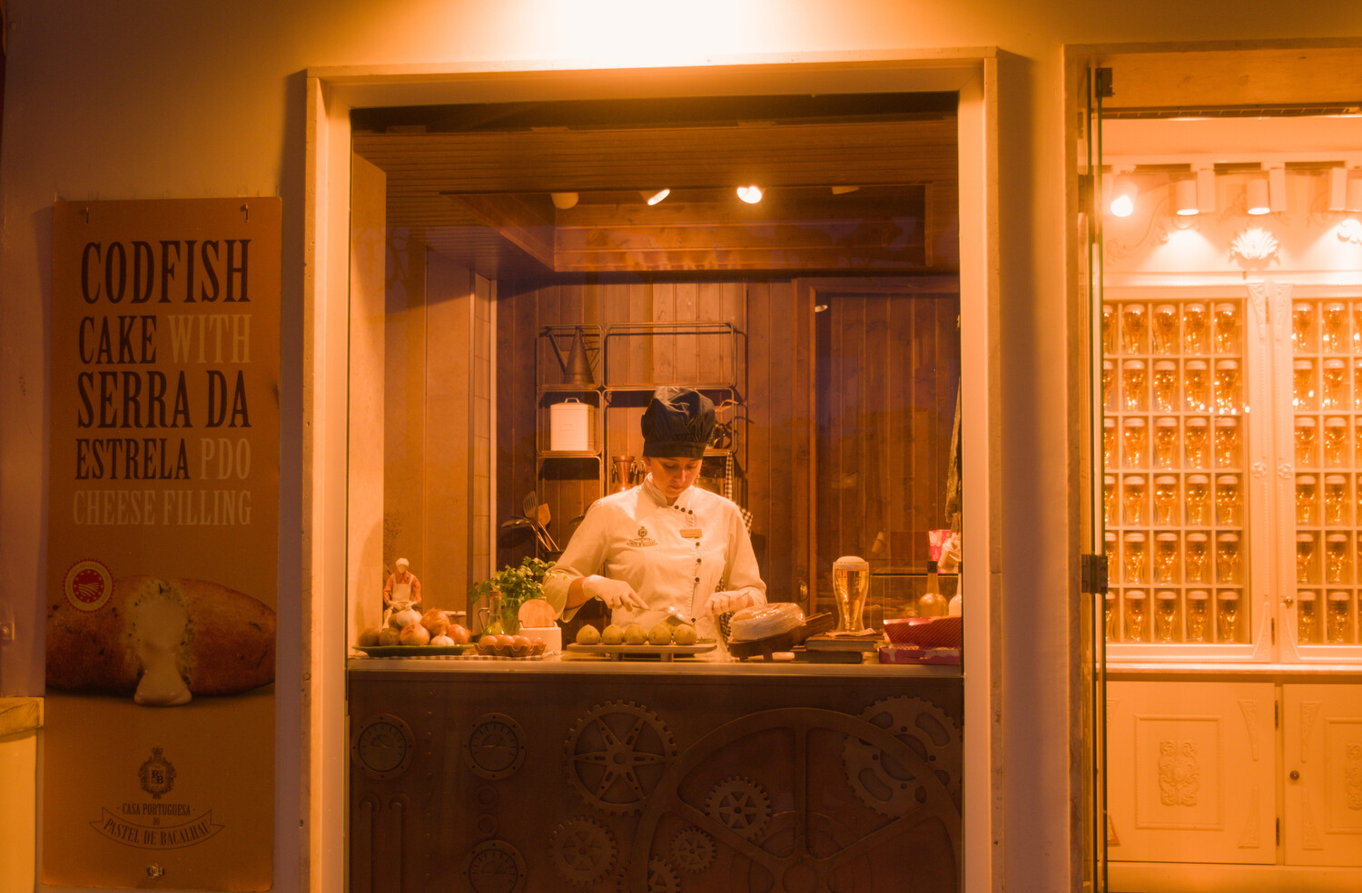 Chef working at counter in warm-lit restaurant window with Portuguese signage and shelving