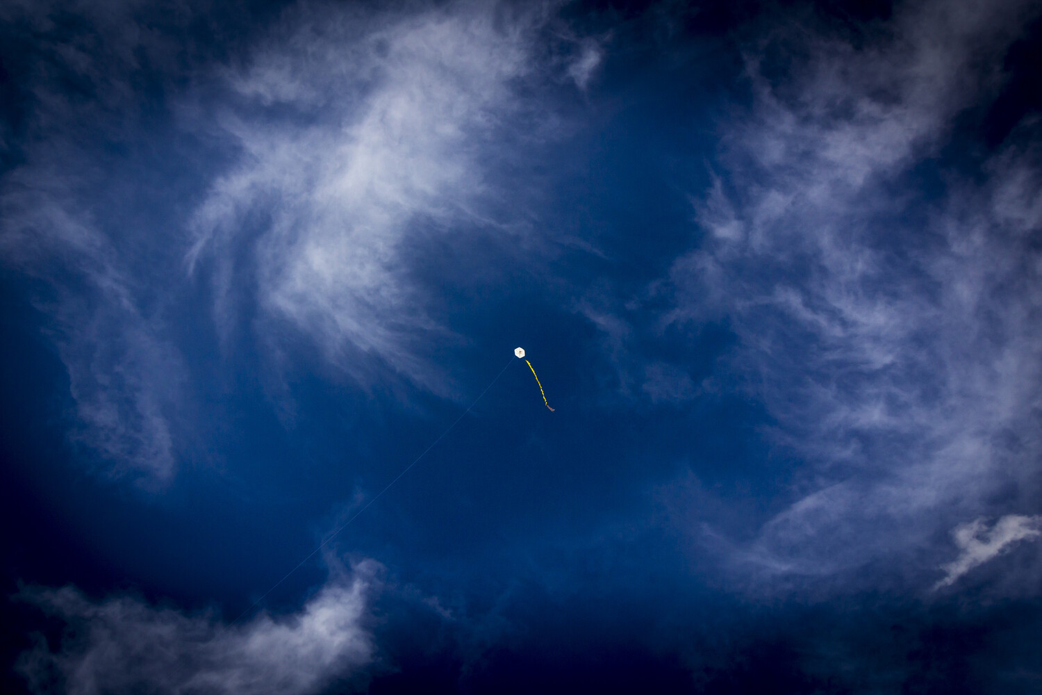 Rocket trail streaking through dramatic cloudy sky against deep blue