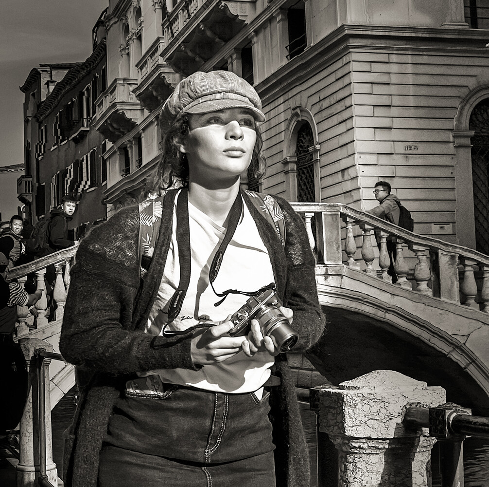 Woman in black jacket and cap standing on Venice bridge, monochrome street photography