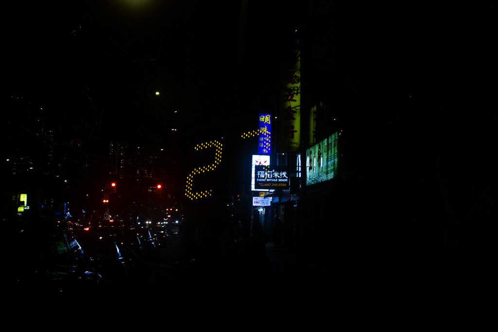 Nighttime cityscape with illuminated buildings and neon signs creating a dark, moody urban scene