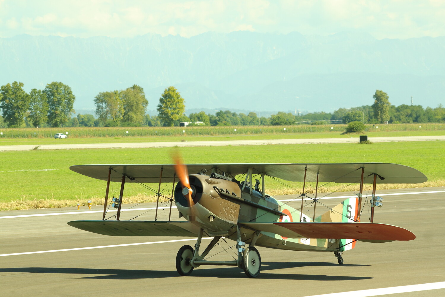 Vintage biplane aircraft parked on an airfield runway with green countryside in background
