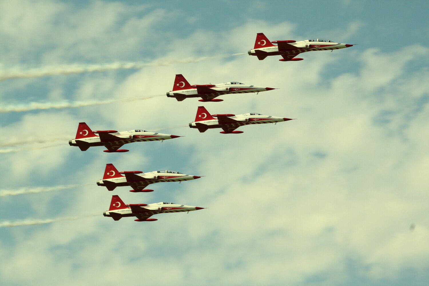 Five military jets in tight formation flying through blue sky with contrails