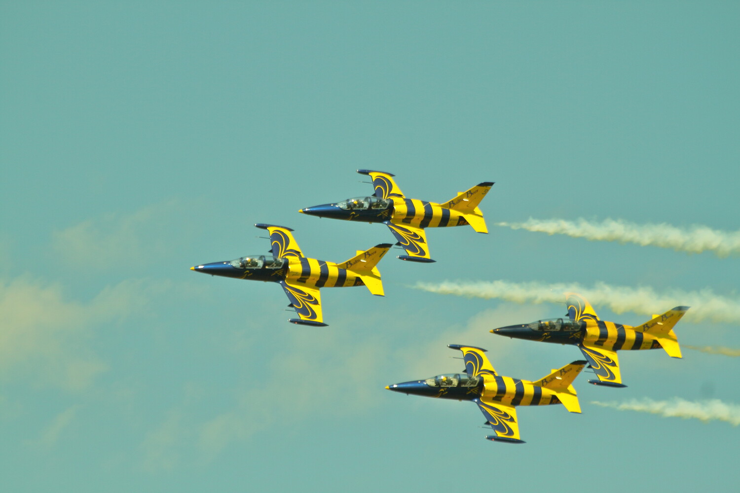 Four military jet aircraft in yellow and black striped livery flying in formation against a turquoise sky