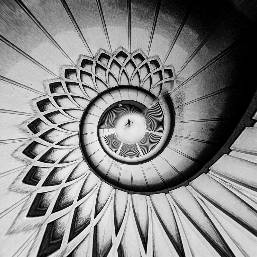 Spiral staircase photographed from below, creating a geometric spiral pattern in black and white