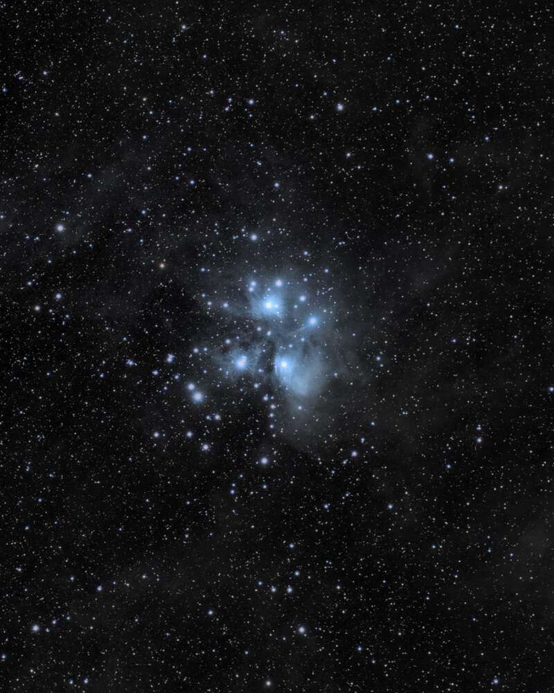 Pleiades star cluster with bright blue stars and nebulosity against dark starfield