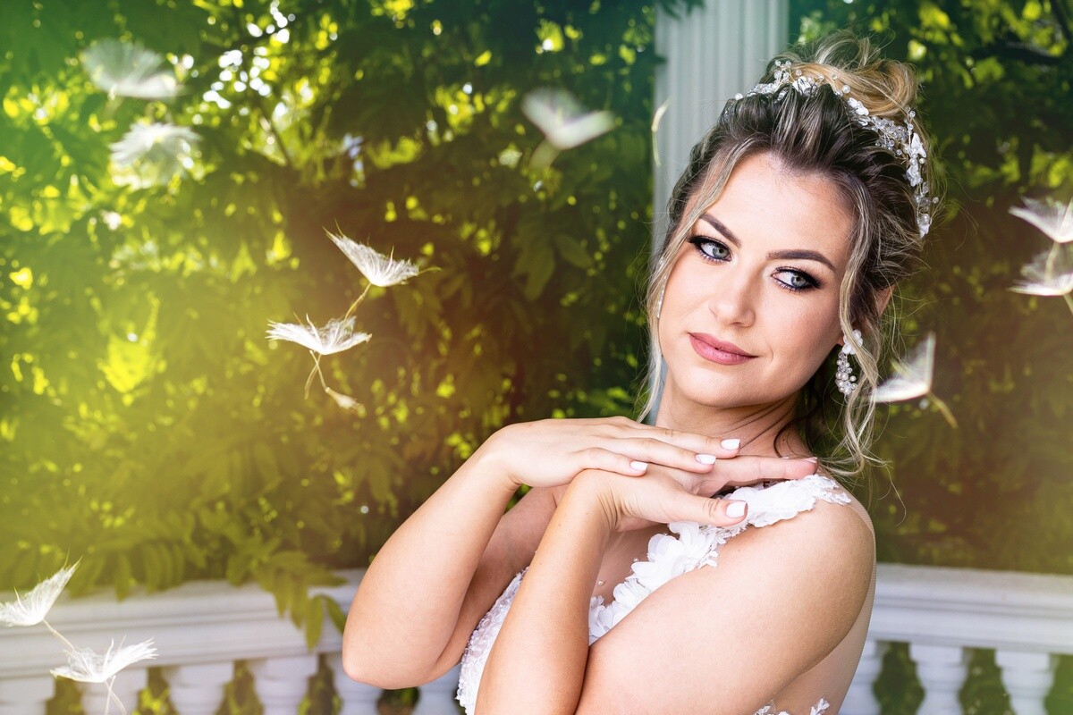 Woman in white lace dress with upswept hair posing against green foliage and white doves in soft natural light