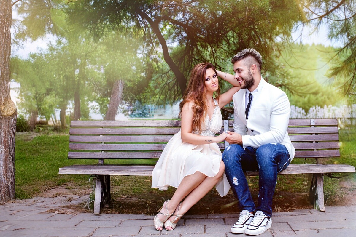 Couple sitting on a park bench under trees, facing each other in conversation