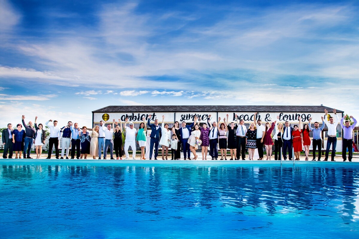 Large group of people standing on a poolside structure overlooking a bright blue swimming pool