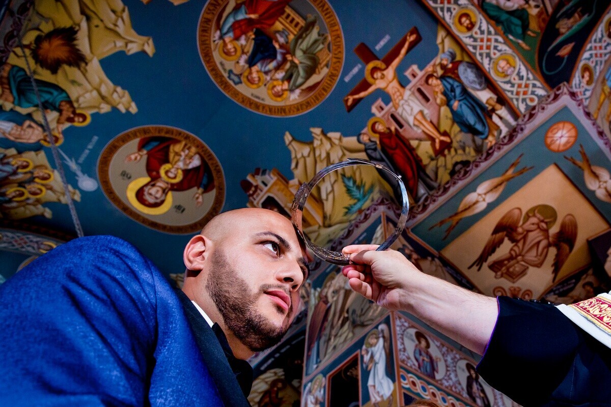 Man in blue shirt gazes upward while pointing at ornate religious iconography on a blue ceiling