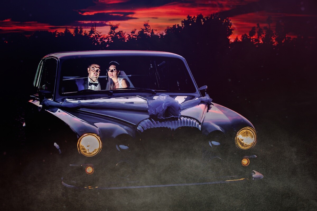 Couple in vintage car at night with dramatic red sunset sky and fog