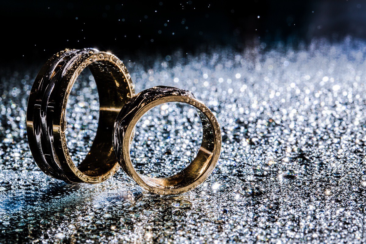 Two gold wedding bands resting on sparkling silver glitter surface with bokeh background