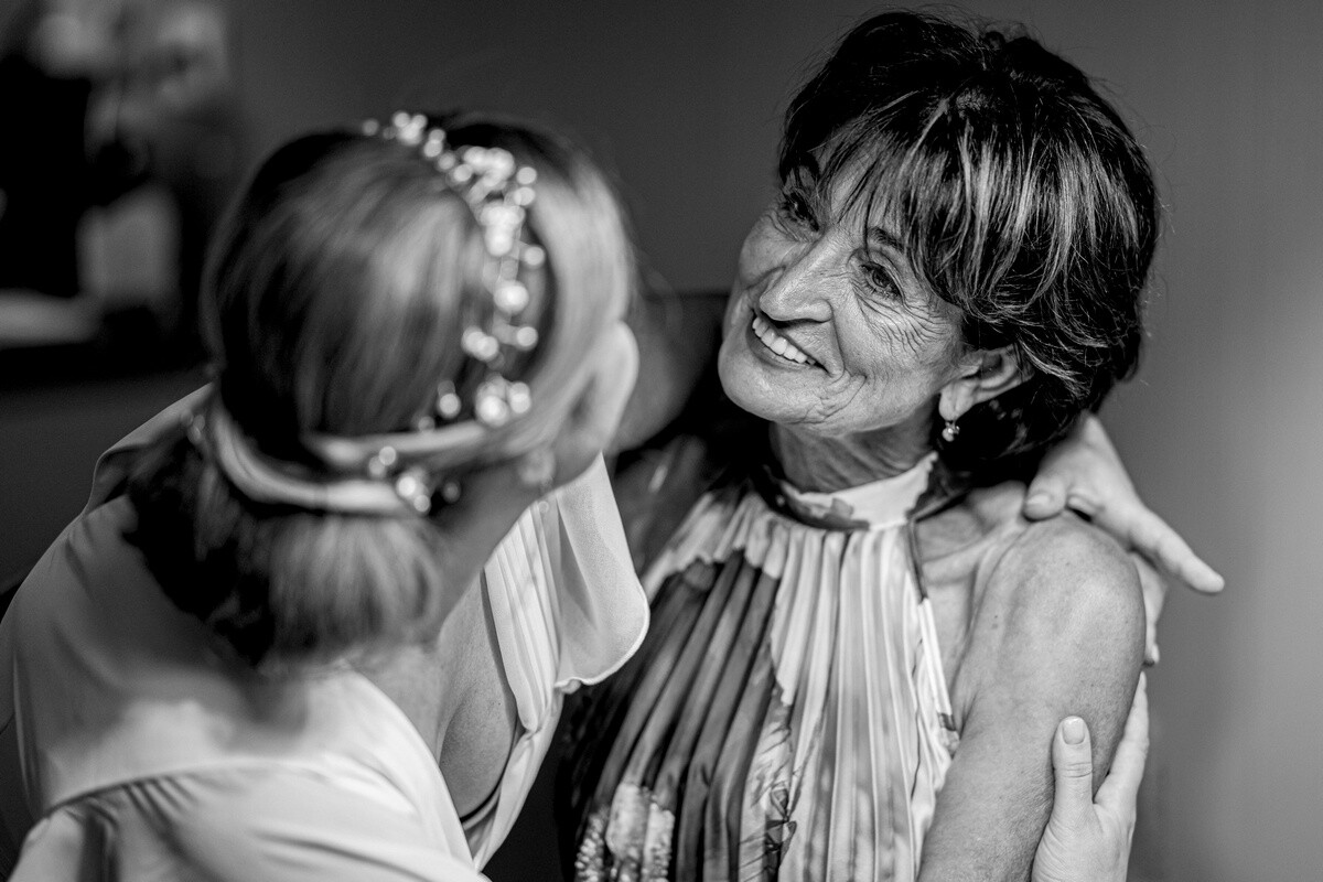 Two women smiling at each other in black and white, one wearing a pearl headpiece