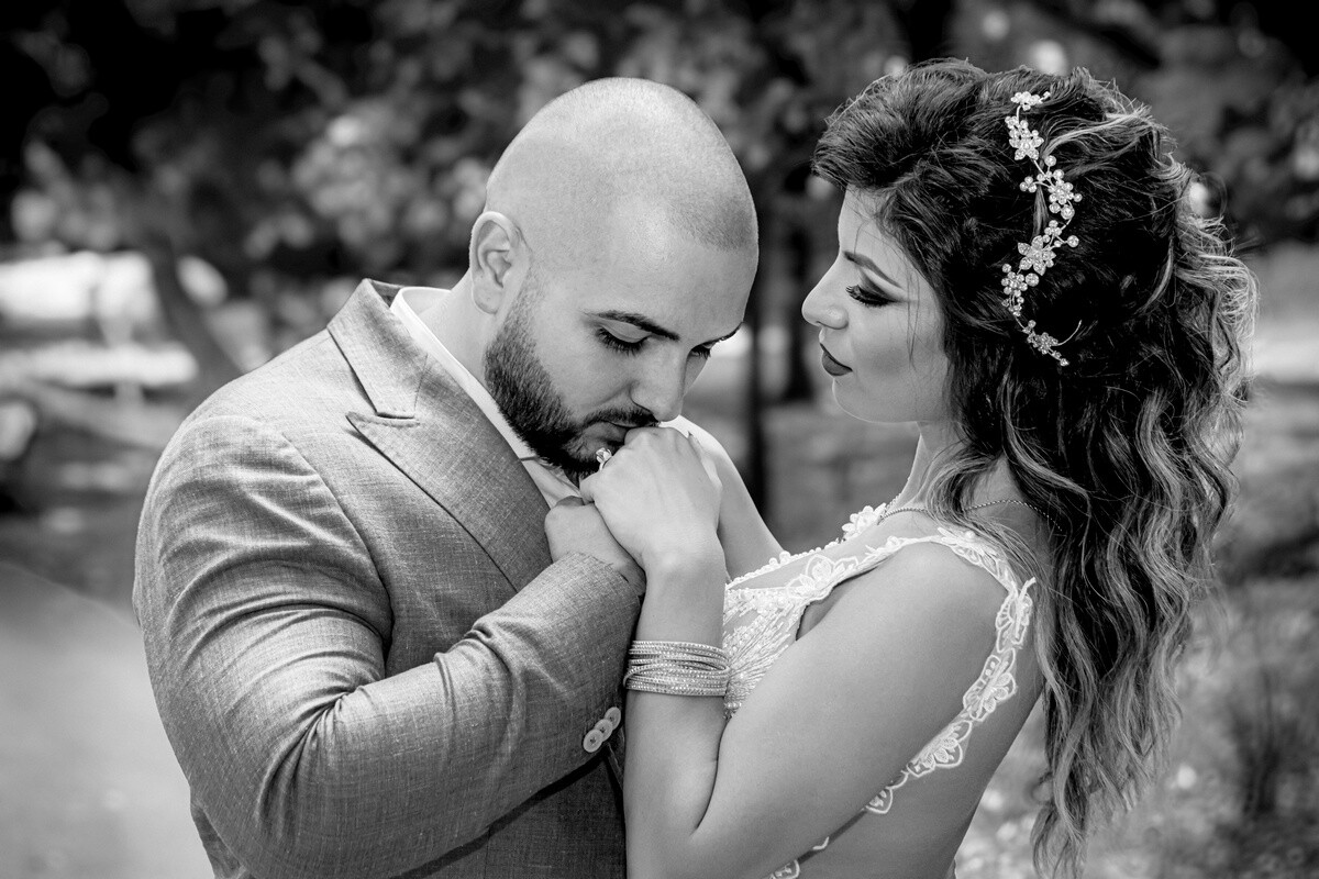Black and white portrait of a bald, bearded man in a suit kissing the hand of a woman with wavy hair and a floral hair piece.