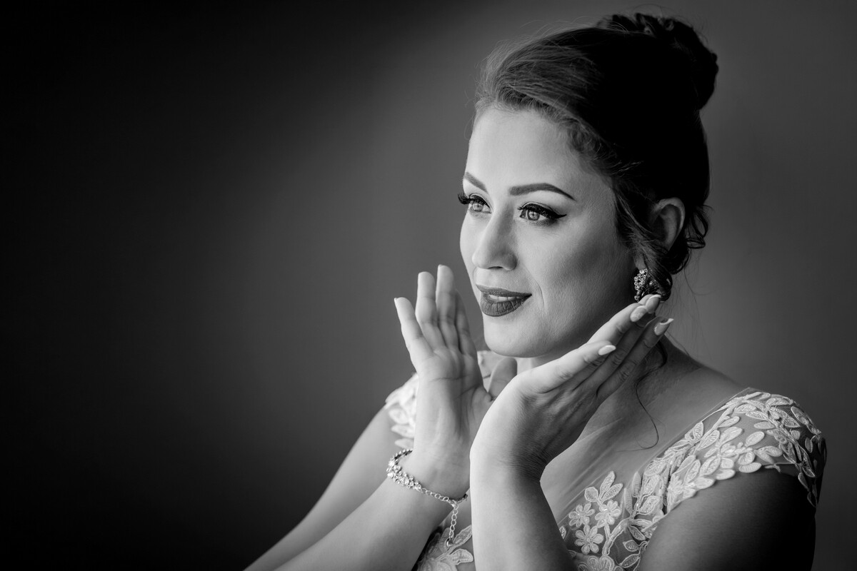 Black and white portrait of a woman in an updo and lace off-shoulder dress, hands raised to her face