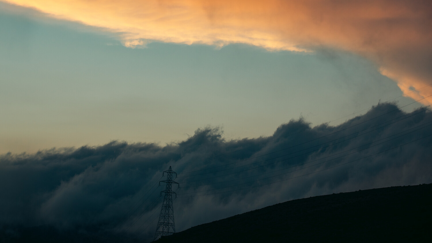 Silhouetted electrical transmission tower against dramatic storm clouds at sunset