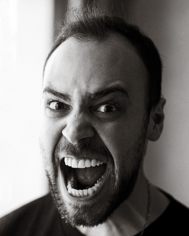 Man with intense expression shouting directly at camera in black and white portrait