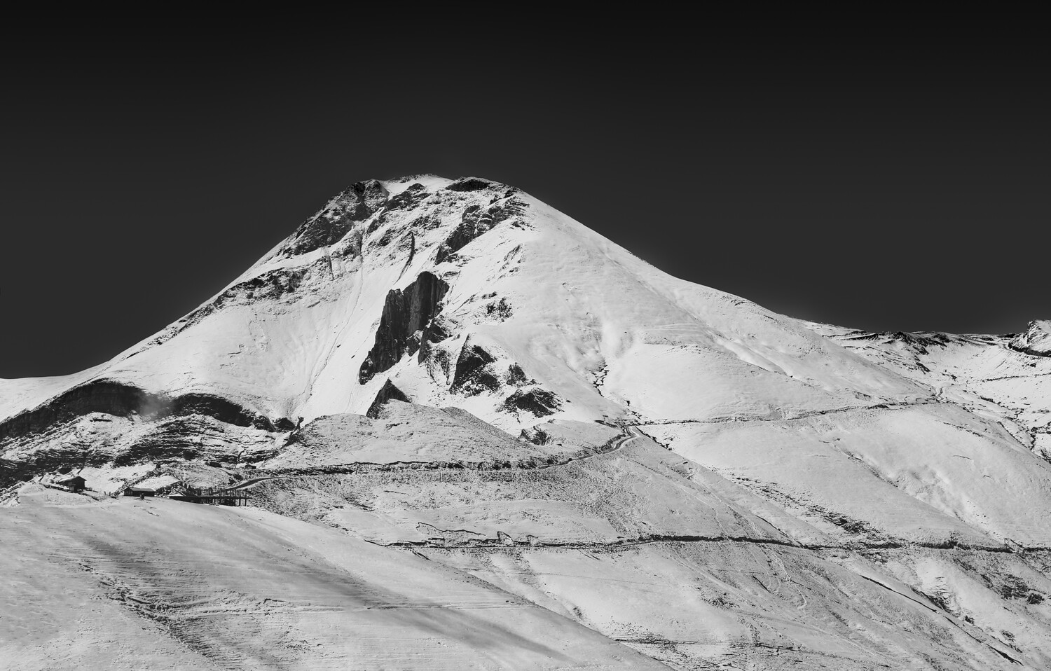 Snow-covered volcanic cone with dark rock outcroppings against dark sky