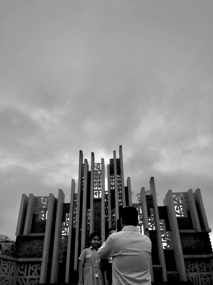 Person standing before towering black architectural spires under dramatic cloudy sky