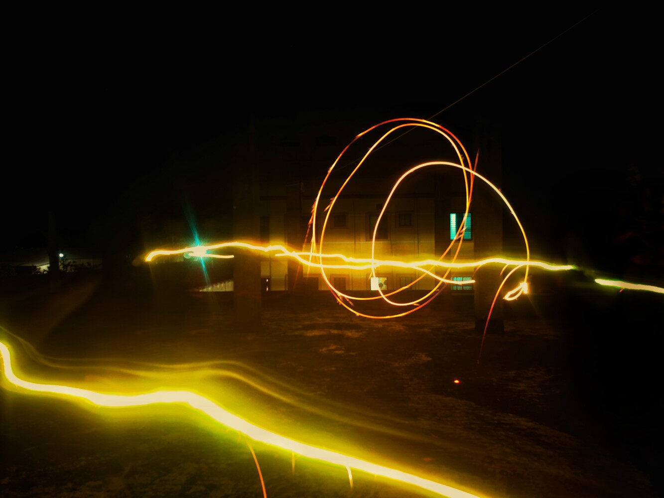 Long exposure light painting with glowing yellow and green neon lines creating circular and curved patterns against dark desert landscape