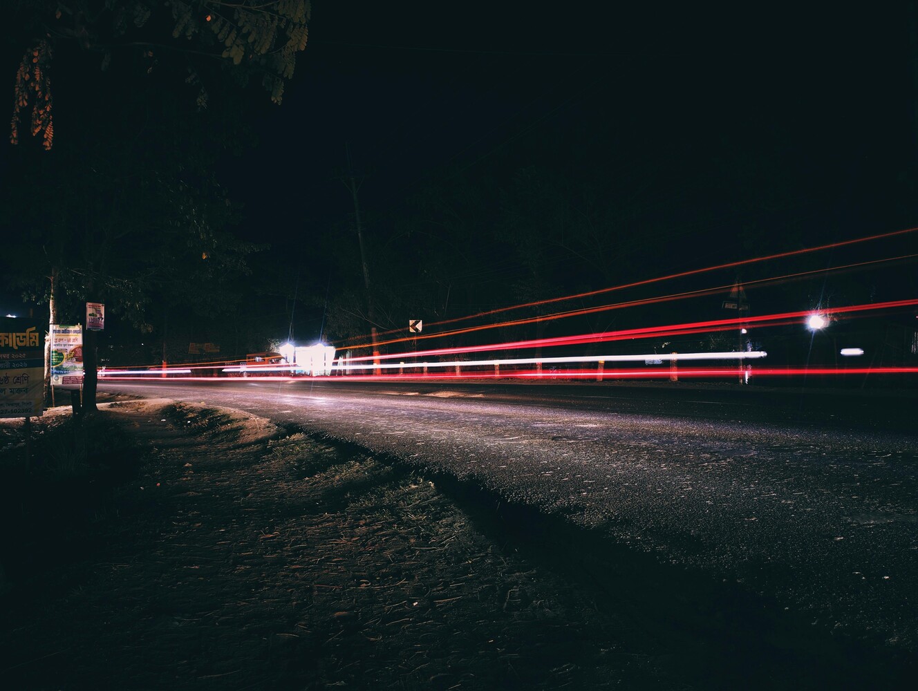 Light trails from a vehicle creating red and white streaks across a dark rural road at night
